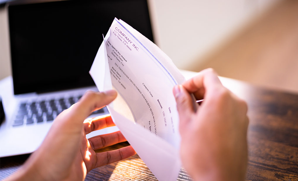 Close up of person opening envelope containing a check