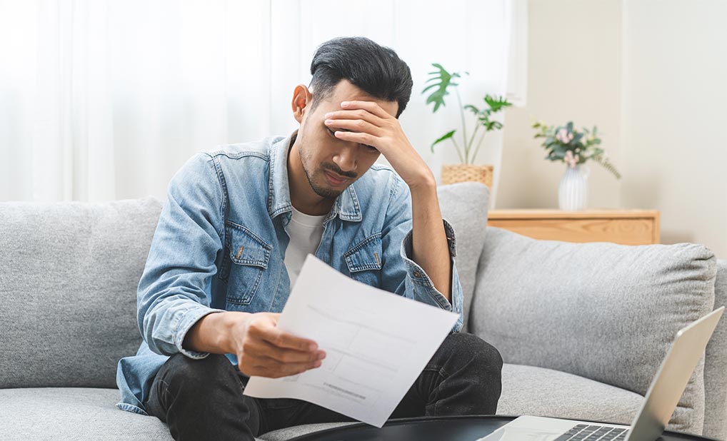 Person looking stressed while holding paper and sitting in front of laptop
