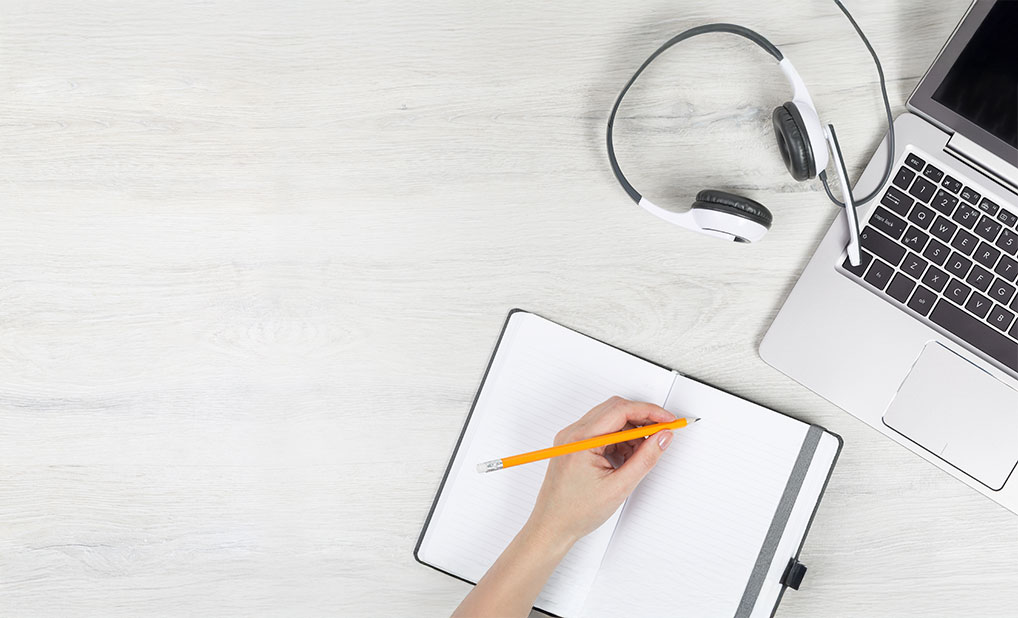 Table with headphones, computer and notebook with someone taking notes