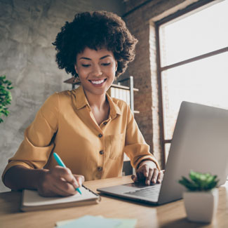 woman typing on a laptop and writing in a notebook