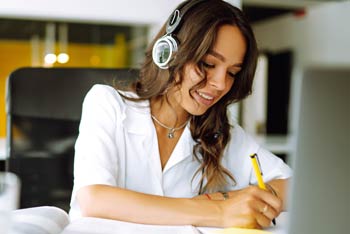 A young woman making notes while listening to a recording